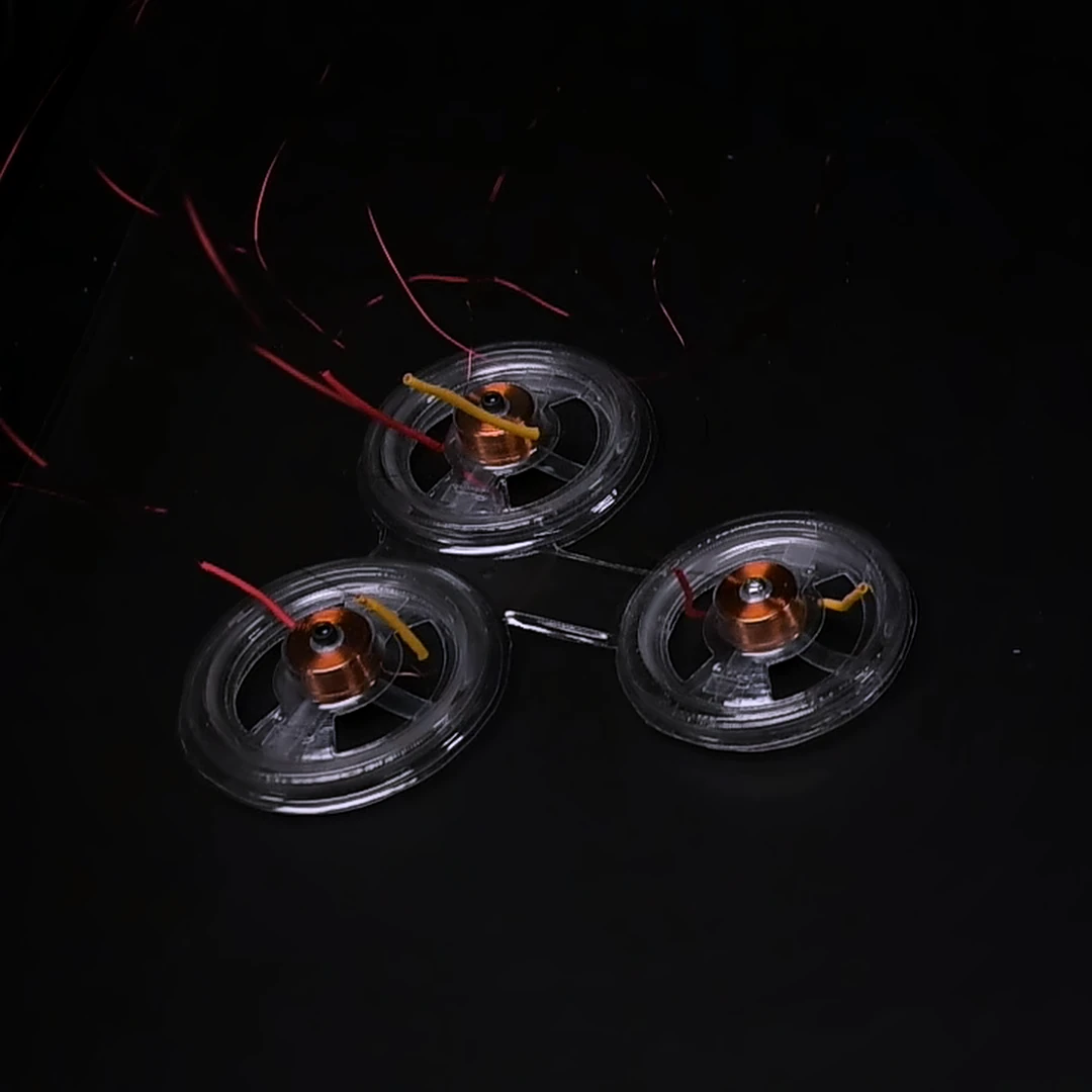 Three BEAMbot modules seen from above during a turning test: clear PETG shells with copper coils at their centers, joined in a triangle and tethered by thin wires, on a black surface.
